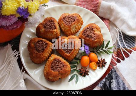 Köstliche Muffins in Herzform sind wunderschön auf einem weißen Teller angeordnet, garniert mit Schokolade, Kumquat und Sternanis Stockfoto