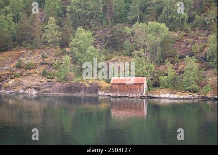 Eine hölzerne Bootshütte am Ufer eines norwegischen Fjords mit Reflexen im Wasser Stockfoto