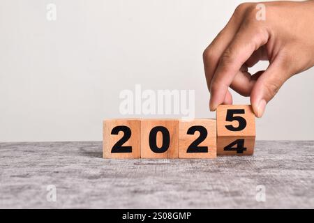 Handumschlag von Holzblöcken von 2024 bis 2025, Geschäftsplanung und Countdown bis 2025. Das Jahr 2024 auf 2025 auf Holzwürfel auf einem Arbeitsauftrag umdrehen Stockfoto