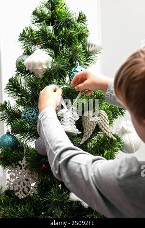 Ein Kind hängt handgemachte weihnachtsschmuck an einem weihnachtsbaum, dekoriert für die Weihnachtszeit. Stockfoto