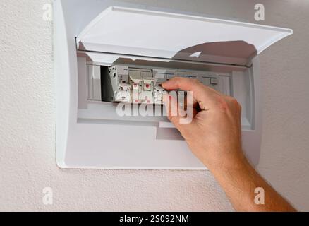 Nahaufnahme eines Elektrikers, der einen Leistungsschalter in einem Sicherungskasten betätigt, um die elektrische Sicherheit und die Stromverteilung zu gewährleisten. Stockfoto