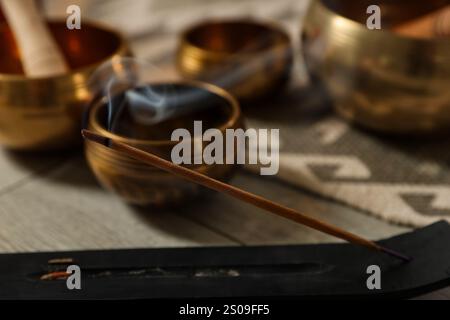 Räucherstäbchen schwelend im Halter und tibetische Klangschalen auf dem Boden, Nahaufnahme Stockfoto