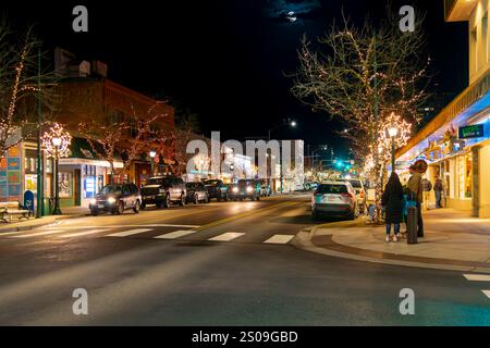 Blick in die Nacht, während Fußgänger die beleuchtete Hauptstraße der Innenstadt von Coeur d'Alene, Idaho, mit beleuchteten Bäumen zur Weihnachtszeit entlang laufen. Stockfoto