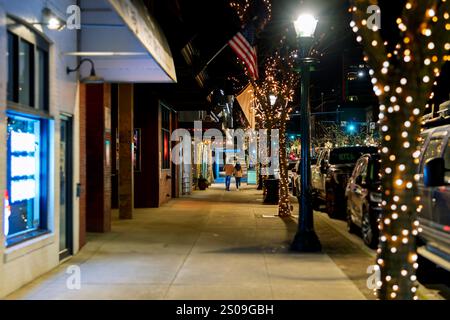 Blick in die Nacht, während Fußgänger die beleuchtete Hauptstraße der Innenstadt von Coeur d'Alene, Idaho, mit beleuchteten Bäumen zur Weihnachtszeit entlang laufen. Stockfoto