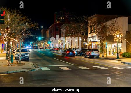 Blick in die Nacht, während Fußgänger die beleuchtete Hauptstraße der Innenstadt von Coeur d'Alene, Idaho, mit beleuchteten Bäumen zur Weihnachtszeit entlang laufen. Stockfoto