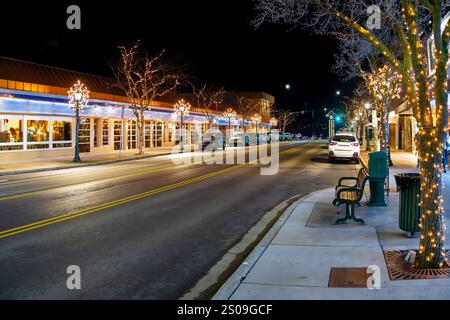 Blick in die Nacht, während Fußgänger die beleuchtete Hauptstraße der Innenstadt von Coeur d'Alene, Idaho, mit beleuchteten Bäumen zur Weihnachtszeit entlang laufen. Stockfoto