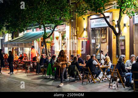 Abends können Sie in den beleuchteten Straßencafés im touristischen Viertel Barrio Santa Cruz der andalusischen Stadt Sevilla, Spanien, speisen. Stockfoto