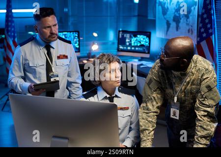 Ernste reife Frau in Uniform, die jungen afroamerikanischen Offizier während der Diskussion vor dem Desktop-Computer ansieht Stockfoto