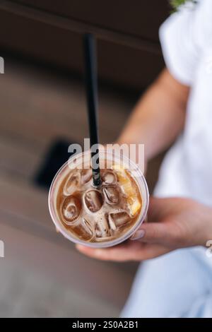 Vertikale Nahaufnahme eines Eisgetränks mit weiblicher Hand und Eiskaffee, der auf der Stadtstraße steht. Frau trinkt kalten Bubble-Tee durch Stockfoto