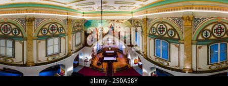 Das Bild zeigt ein Kircheninnere mit einer reich verzierten Decke, komplizierten Mustern und einem Wandgemälde über dem Altar. Verzierte Säulen und Buntglas A Stockfoto