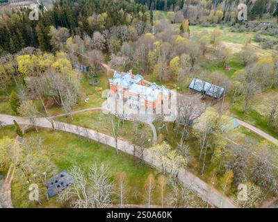 Aus der Vogelperspektive ist ein großes Ziegelhaus mit symmetrischem Design, umgeben von Laub- und Nadelbäumen, offenen Grasflächen und nea Stockfoto