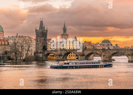 Prag, Tschechische Republik - 20. Dezember 2024: Karlsbrücke mit Altstadtturm auf der Moldau mit Touristenboot unter farbenfrohem Sonnenuntergang Stockfoto