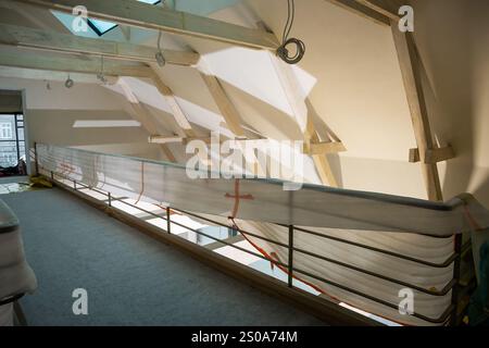 Ein Loft-Bereich im Bau verfügt über freiliegende Holzbalken und eine schräge Decke. Das natürliche Licht eines Oberlichts wirft geometrische Schatten auf die Wände Stockfoto