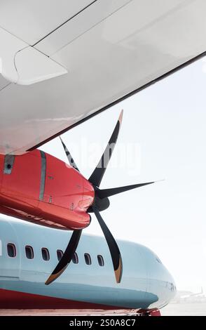 Blick unter einem Flügel eines blauen Turboprop-Flugzeugs mit roten Streifen und Motorverkleidungen. Passagierflugzeug mit Propellermotor. Stockfoto