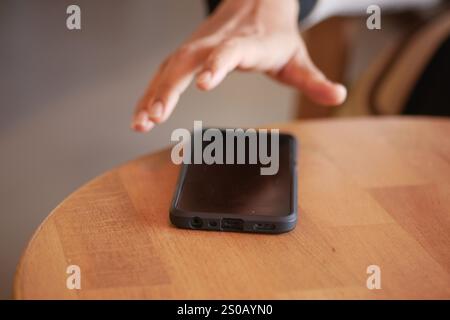 Eine Hand, die das Handy auf dem Tisch abnimmt. Stockfoto