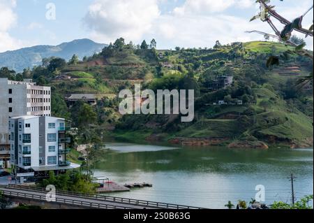 Ruhiger See eingebettet in üppig grüne Hügel, moderne Gebäude verleihen der Landschaft einen Hauch von zeitgenössischem Charme. Stockfoto