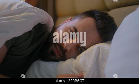 Kaukasischer Mann, der im Bett liegt Schlafzimmer Schlaflosigkeit Frustration nachdenkliche Angst männliche Schlafenszeit Gesicht Hypothekenvermietung melancholisch traurig traurig müde Stockfoto