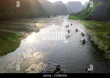 Luftdrohne, die von der Landschaft von Ninh Binh mit riesigen Kalksteinklippen und Fluss umgeben von grünen Feldern zu traditionellem Holz schwenkt Stockfoto