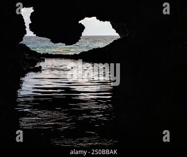 Ein Blick aus dem Inneren einer Höhle mit Blick auf das Meer. Der Höhleneingang umrahmt das Meer mit sanften Wellen, die Licht auf die Wasseroberfläche reflektieren. Stockfoto