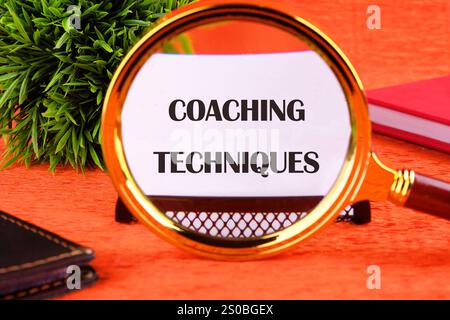Konzept von Business und Entwicklung. Konzeptionelle Text-COACHING-TECHNIKEN auf einer weißen Karte auf orangefarbenem Hintergrund durch eine Lupe geschrieben. Stockfoto