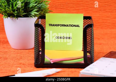 Geschäfts-, Formations- oder Transformationskonzept. Kopierbereich. TRANSFORMIERENDES COACHING auf einem grünen Aufkleber in einem Ständer auf orangefarbenem Hintergrund. Stockfoto