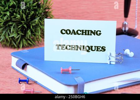 Konzept von Business und Entwicklung. Konzeptionelle COACHING-TECHNIKEN auf einer weißen Karte, die auf einem Geschäftstagebuch auf orangem Hintergrund steht. Stockfoto