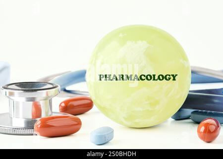 Eine hellgrüne Kugel mit dem Wort Pharmakologie sitzt zwischen bunten Tabletten und einem Stethoskop auf einer weißen Oberfläche, was das Studium der Medizin hervorhebt Stockfoto