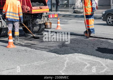 Straßenarbeiter reparieren Asphaltbelag an hellen Tagen in städtischen Umgebungen Stockfoto