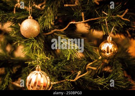 Nahaufnahmen von Weihnachtsbaumschmuck mit goldenen, lila und rosa Kugeln, die unter warmem Licht leuchten. Die festliche Dekoration sorgt für ein gemütliches und Stockfoto
