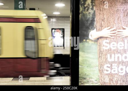 Auf einer Werbetafel am Bahnsteig S-Bahn ist ein Baum zu sehen, der umarmt wird und der Schriftzug Seele und Säge teilweise abgebildet wird. IMH Hintergrund fährt bewegungsunscharf eine S-Bahn ein. Werbung am Bahnsteig Berlin Anhalter Bahnhof *** auf einer Werbetafel auf dem Bahnsteig der S-Bahn ist ein Baum umfaßt und die Schrift Seele und Säge teilweise im Hintergrund abgebildet, eine S-Bahn kommt unbeweglich an Werbung auf dem Bahnsteig Berlin Anhalter Bahnhof Stockfoto