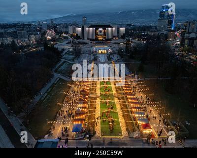 Nächtliche Luftaufnahme des Nationalen Kulturpalastes (NDK) in Sofia, Bulgarien, mit beleuchteten Weihnachtsmarktständen, lebhaften Lichtern der Stadt und Stockfoto