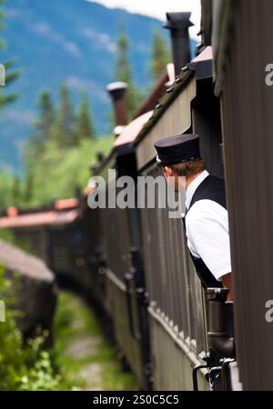Skagway Alaska, Zugbegleiter der White Pass and Yukon Route Railway, beugt sich zwischen den Autos und bietet eine bessere Aussicht. Stockfoto