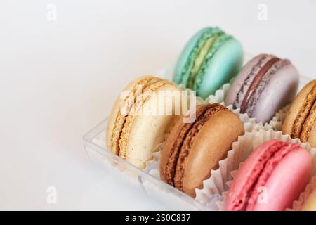 Französische Macarons mit weißer Paperpan in transparenter Plastikverpackung auf grauem Hintergrund, bunte Kuchen mit verschiedenen Geschmacksrichtungen. Appetitliches Dessert, Makronen. Kopierbereich für Text, Draufsicht Stockfoto