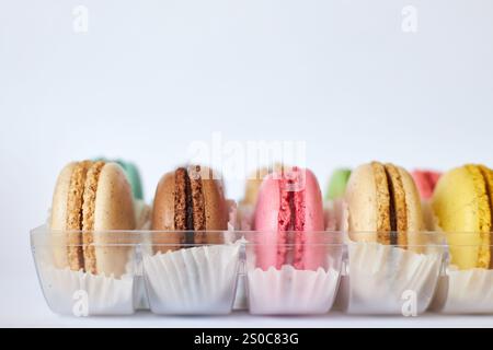 Französische Macarons mit weißer Paperpan in transparenter Plastikverpackung auf grauem Hintergrund, bunte Kuchen mit verschiedenen Geschmacksrichtungen. Appetitliches Dessert, Makronen. Kopierraum für Text, Seitenansicht Stockfoto