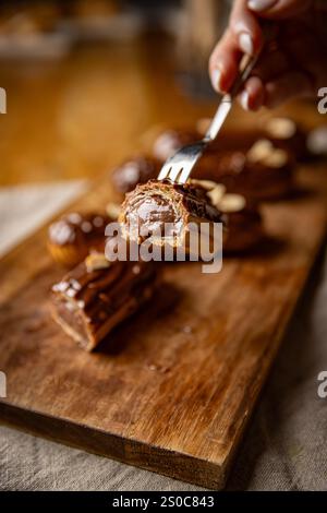 Frisch zubereitete Schokoladen-Eclairs werden mit Schokoladenglasur belegt, die auf einem Holzbrett serviert wird Stockfoto