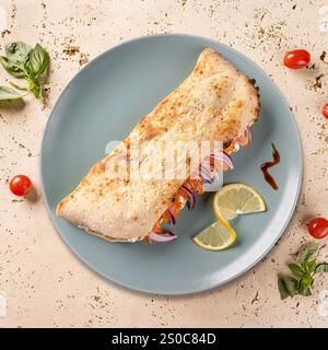 Köstliche geschlossene Calzone Pizza mit Lachs, Frischkäse, roten Zwiebeln und Zitronenscheiben auf elegantem Teller Stockfoto