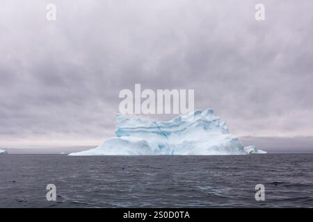 Dieses atemberaubende Bild fängt einen herrlichen Eisberg ein, der im Sommer vor der Küste Grönlands im Ozean schwimmt. Der strahlend blaue Himmel verbessert den Stockfoto
