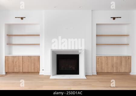Ein Kamin mit eingebauten Regalen und Böden aus weißer Eiche, schwarze Lichter über den Regalen und weiße Zierleisten um den Kamin. Stockfoto