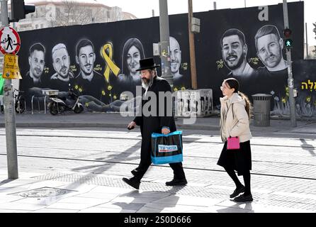 Jerusalem, Israel. Dezember 2024. Ein Ultra-orthodoxer Mann geht vor einem Graffiti-Wandgemälde mit den Gesichtern israelischer Geiseln, die die Hamas am 448. Tag des Hamas-israelischen Krieges in Gaza festgehalten hat, am Freitag, den 27. Dezember 2024 in Jerusalem. Familien von Geiseln drohten rechtliche Schritte gegen den israelischen Ministerpräsidenten Benjamin Netanjahu und beschuldigten ihn, ihre Angehörigen im Stich zu lassen und einen Waffenstillstand und eine Freilassung von Geiseln zu blockieren. In Gaza werden noch 100 Geiseln festgehalten, und viele sind bekanntermaßen tot. Foto: Debbie Hill/ Credit: UPI/Alamy Live News Stockfoto