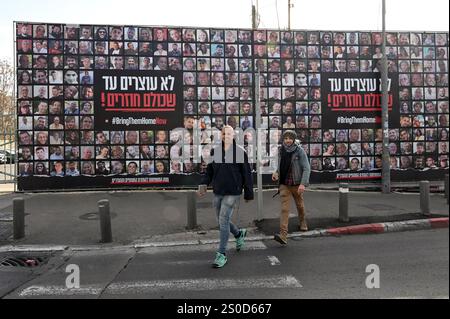 Jerusalem, Israel. Dezember 2024. Ein Mann läuft an einer großen Plakatwand mit der Aufschrift "#BRINGTHEMHOMENOW" vorbei, auf der die Gesichter israelischer Geiseln dargestellt sind, die die Hamas am 448. Tag des Hamas-israelischen Krieges in Gaza festgehalten hat, am Freitag, den 27. Dezember 2024, in Jerusalem. Familien von Geiseln drohten rechtliche Schritte gegen den israelischen Ministerpräsidenten Benjamin Netanjahu und beschuldigten ihn, ihre Angehörigen im Stich zu lassen und einen Waffenstillstand und eine Freilassung von Geiseln zu blockieren. In Gaza werden noch 100 Geiseln festgehalten, und viele sind bekanntermaßen tot. Foto: Debbie Hill/ Credit: UPI/Alamy Live News Stockfoto