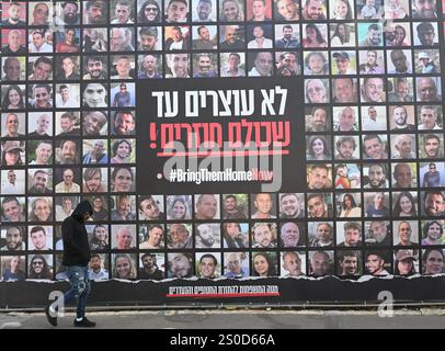 Jerusalem, Israel. Dezember 2024. Ein Mann läuft an einer großen Plakatwand mit der Aufschrift "#BRINGTHEMHOMENOW" vorbei, auf der die Gesichter israelischer Geiseln dargestellt sind, die die Hamas am 448. Tag des Hamas-israelischen Krieges in Gaza festgehalten hat, am Freitag, den 27. Dezember 2024, in Jerusalem. Familien von Geiseln drohten rechtliche Schritte gegen den israelischen Ministerpräsidenten Benjamin Netanjahu und beschuldigten ihn, ihre Angehörigen im Stich zu lassen und einen Waffenstillstand und eine Freilassung von Geiseln zu blockieren. In Gaza werden noch 100 Geiseln festgehalten, und viele sind bekanntermaßen tot. Foto: Debbie Hill/ Credit: UPI/Alamy Live News Stockfoto