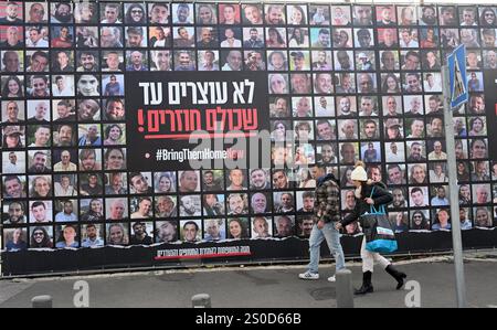 Jerusalem, Israel. Dezember 2024. Ein Mann läuft an einer großen Plakatwand mit der Aufschrift "#BRINGTHEMHOMENOW" vorbei, auf der die Gesichter israelischer Geiseln dargestellt sind, die die Hamas am 448. Tag des Hamas-israelischen Krieges in Gaza festgehalten hat, am Freitag, den 27. Dezember 2024, in Jerusalem. Familien von Geiseln drohten rechtliche Schritte gegen den israelischen Ministerpräsidenten Benjamin Netanjahu und beschuldigten ihn, ihre Angehörigen im Stich zu lassen und einen Waffenstillstand und eine Freilassung von Geiseln zu blockieren. In Gaza werden noch 100 Geiseln festgehalten, und viele sind bekanntermaßen tot. Foto: Debbie Hill/ Credit: UPI/Alamy Live News Stockfoto