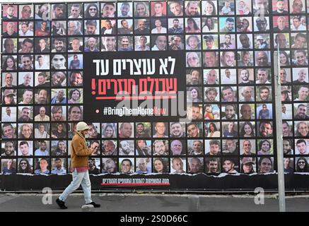 Jerusalem, Israel. Dezember 2024. Ein Mann läuft an einer großen Plakatwand mit der Aufschrift "#BRINGTHEMHOMENOW" vorbei, auf der die Gesichter israelischer Geiseln dargestellt sind, die die Hamas am 448. Tag des Hamas-israelischen Krieges in Gaza festgehalten hat, am Freitag, den 27. Dezember 2024, in Jerusalem. Familien von Geiseln drohten rechtliche Schritte gegen den israelischen Ministerpräsidenten Benjamin Netanjahu und beschuldigten ihn, ihre Angehörigen im Stich zu lassen und einen Waffenstillstand und eine Freilassung von Geiseln zu blockieren. In Gaza werden noch 100 Geiseln festgehalten, und viele sind bekanntermaßen tot. Foto: Debbie Hill/ Credit: UPI/Alamy Live News Stockfoto