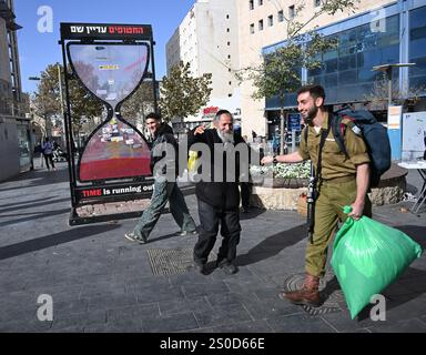 Jerusalem, Israel. Dezember 2024. Ein orthodoxer Mann tanzt vor einer Sanduhr mit der Aufschrift "DIE ZEIT läuft ab" für die israelischen Geiseln, die die Hamas am 448. Tag des Hamas-israelischen Krieges in Gaza festgehalten hat, am Freitag in Jerusalem, dem 27. Dezember 2024. Familien von Geiseln drohten rechtliche Schritte gegen den israelischen Ministerpräsidenten Benjamin Netanjahu und beschuldigten ihn, ihre Angehörigen im Stich zu lassen und einen Waffenstillstand und eine Freilassung von Geiseln zu blockieren. In Gaza werden noch 100 Geiseln festgehalten, und viele sind bekanntermaßen tot. Foto: Debbie Hill/ Credit: UPI/Alamy Live News Stockfoto