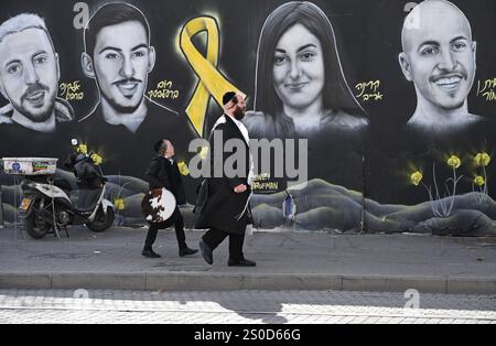 Jerusalem, Israel. Dezember 2024. Ein Ultra-orthodoxer Mann und Junge spazieren an einem Graffiti-Wandgemälde mit den Gesichtern israelischer Geiseln vorbei, die die Hamas am 448. Tag des Hamas-israelischen Krieges in Gaza festgehalten hat, am Freitag, den 27. Dezember 2024 in Jerusalem. Familien von Geiseln drohten rechtliche Schritte gegen den israelischen Ministerpräsidenten Benjamin Netanjahu und beschuldigten ihn, ihre Angehörigen im Stich zu lassen und einen Waffenstillstand und eine Freilassung von Geiseln zu blockieren. In Gaza werden noch 100 Geiseln festgehalten, und viele sind bekanntermaßen tot. Foto: Debbie Hill/ Credit: UPI/Alamy Live News Stockfoto