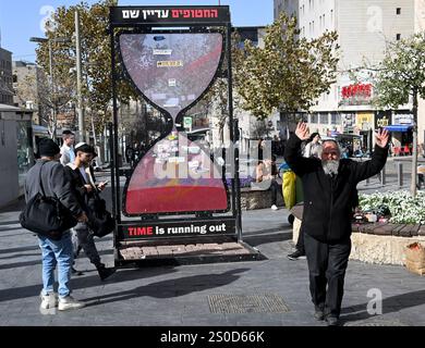 Jerusalem, Israel. Dezember 2024. Ein orthodoxer Mann tanzt vor einer Sanduhr mit der Aufschrift "DIE ZEIT läuft ab" für die israelischen Geiseln, die die Hamas am 448. Tag des Hamas-israelischen Krieges in Gaza festgehalten hat, am Freitag in Jerusalem, dem 27. Dezember 2024. Familien von Geiseln drohten rechtliche Schritte gegen den israelischen Ministerpräsidenten Benjamin Netanjahu und beschuldigten ihn, ihre Angehörigen im Stich zu lassen und einen Waffenstillstand und eine Freilassung von Geiseln zu blockieren. In Gaza werden noch 100 Geiseln festgehalten, und viele sind bekanntermaßen tot. Foto: Debbie Hill/ Credit: UPI/Alamy Live News Stockfoto