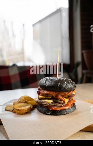 Großer appetitlicher Burger mit schwarzem Brötchen auf dem Tisch im Café. Kopierbereich Stockfoto