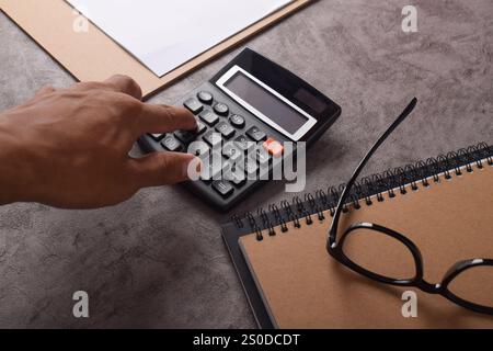 Nahaufnahme einer Person, die den Gewinn berechnet. Notizbuch, Brille und Taschenrechner liegen auf dem Tisch. Finanzkonzept Stockfoto