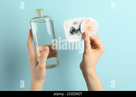 Frau mit mizellarem Wasser und schmutzigen Wattepads auf hellblauem Hintergrund, Nahaufnahme Stockfoto