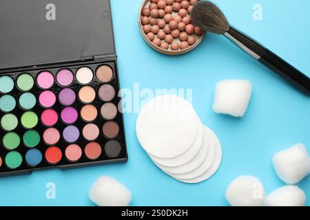 Wattepads, Bällchen, Lidschatten, Rouge und Pinsel auf hellblauem Hintergrund, flach gelegt Stockfoto